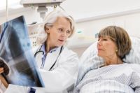 Ärztin zeigt auf Station Patientin im Bett Röntgen